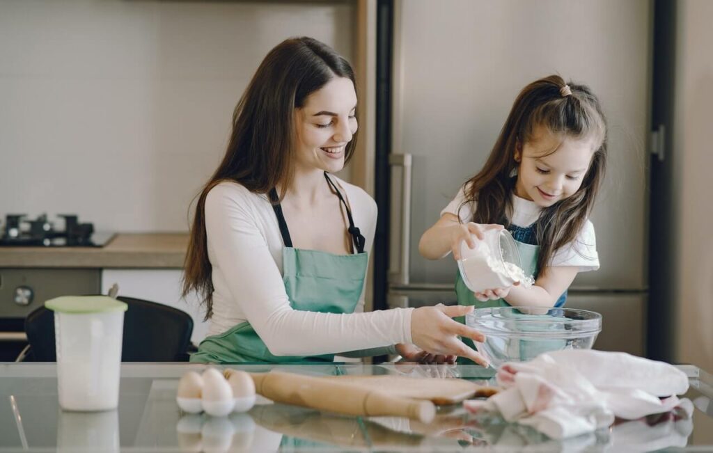 Girl pouring flour in bowl with mother