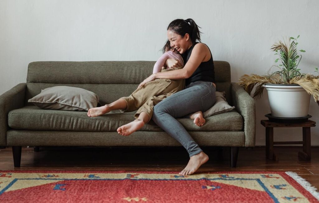 Mother sitting on couch, laughing and hugging her child