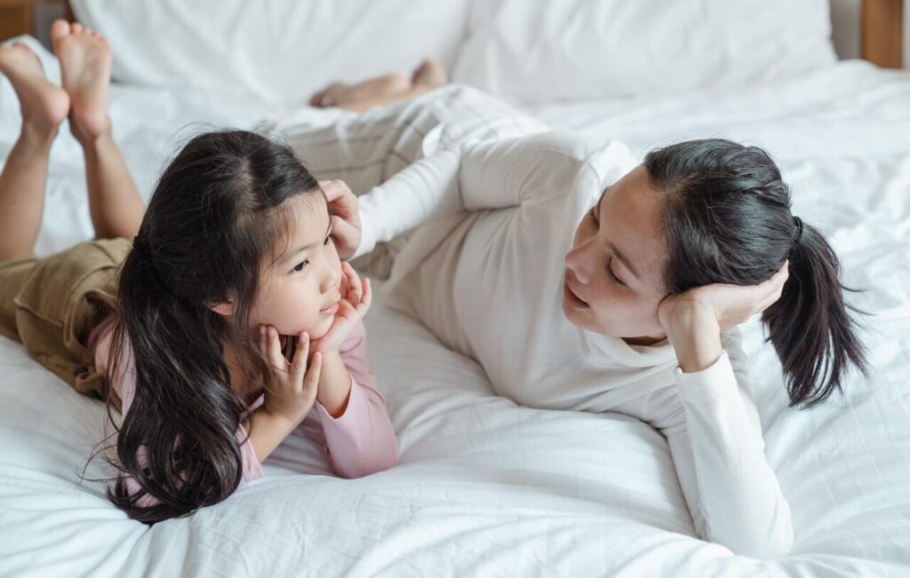 Woman and girl lying on bed and taking with interest