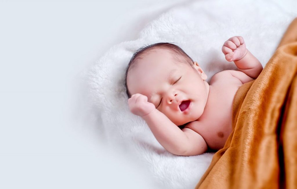 Image of a Newborn baby lying on fur pillow in brown blanket