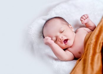 Image of a Newborn baby lying on fur pillow in brown blanket