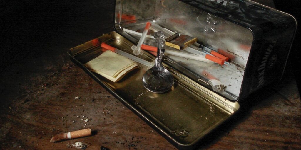 A tin box with drugs, syringes, and substance