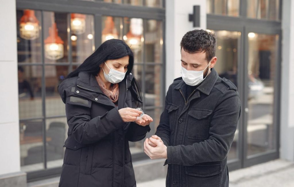Image of Young couple wearing masks disinfecting hands