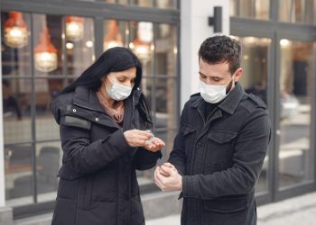 Image of Young couple wearing masks disinfecting hands