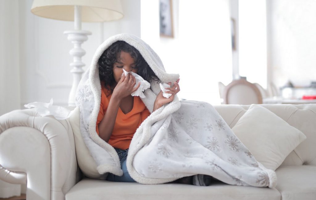 Image of a young ethnic woman sitting on sofa having coronavirus symptoms of flu and body chills