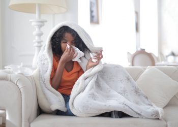 Image of a young ethnic woman sitting on sofa having coronavirus symptoms of flu and body chills