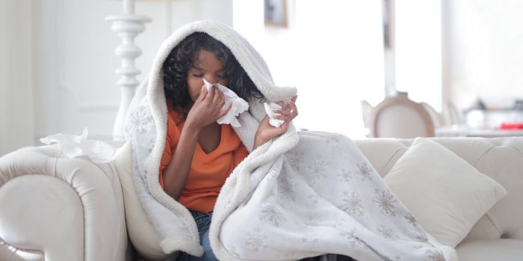 Coronavirus Symptoms Persist For Three Weeks, Says CDC 1 Image of a young ethnic woman sitting on sofa having coronavirus symptoms of flu and body chills