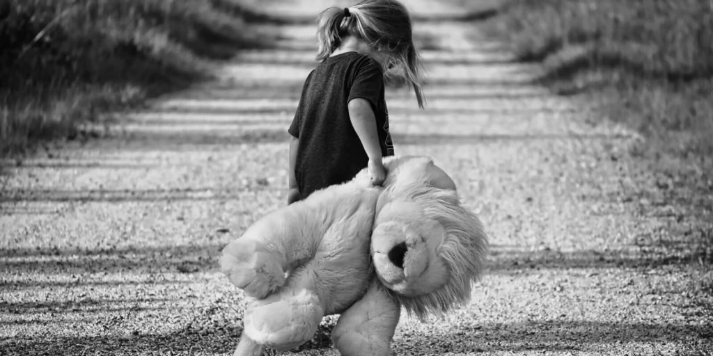 Image of sad Child walking on road holding a teddy bear