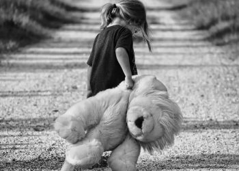 Image of sad Child walking on road holding a teddy bear