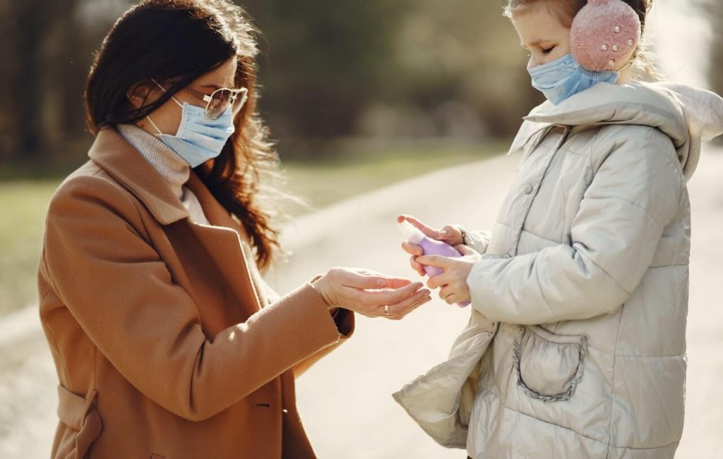 Image of daughter spraying antiseptic on hands of mother