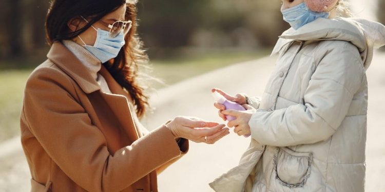 Image of daughter spraying antiseptic on hands of mother