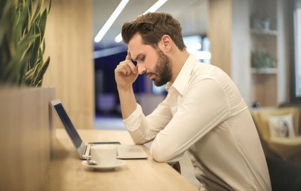 Image of man with hand on head and looking at laptop