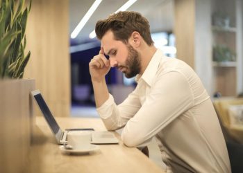 Image of man with hand on head and looking at laptop