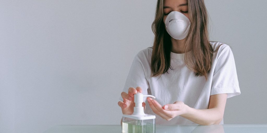 Image of a woman in white shirt, wearing a masks and using hand sanitizer