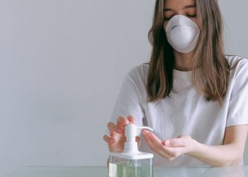 Image of a woman in white shirt, wearing a masks and using hand sanitizer