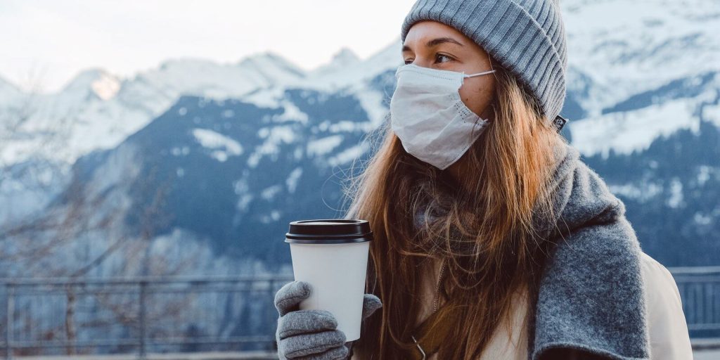 Image of a Woman wearing warm clothes and mask in winters holding a coffee cup