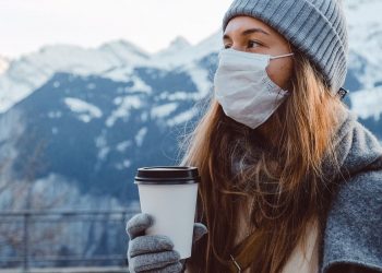 Image of a Woman wearing warm clothes and mask in winters holding a coffee cup