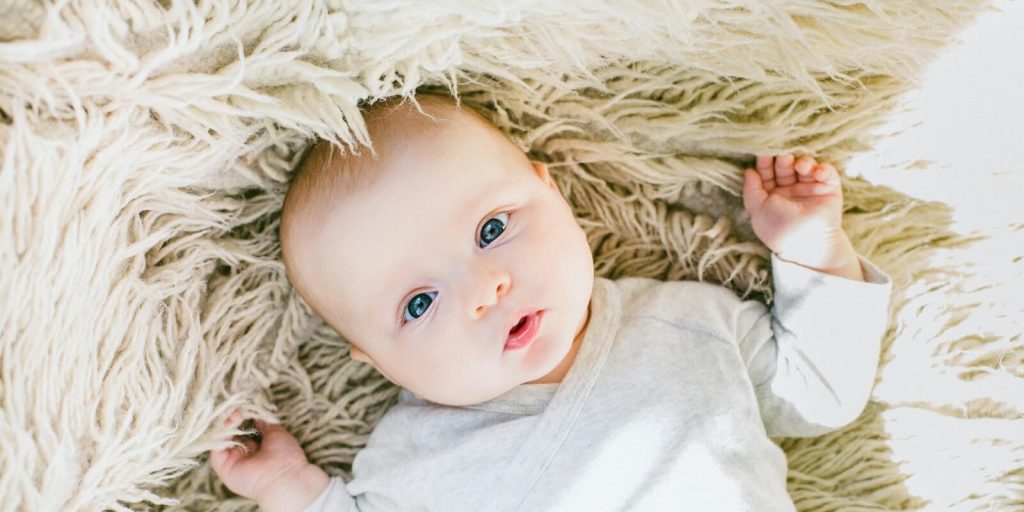 Image of an infant baby wearing white onesie and lying in the bed