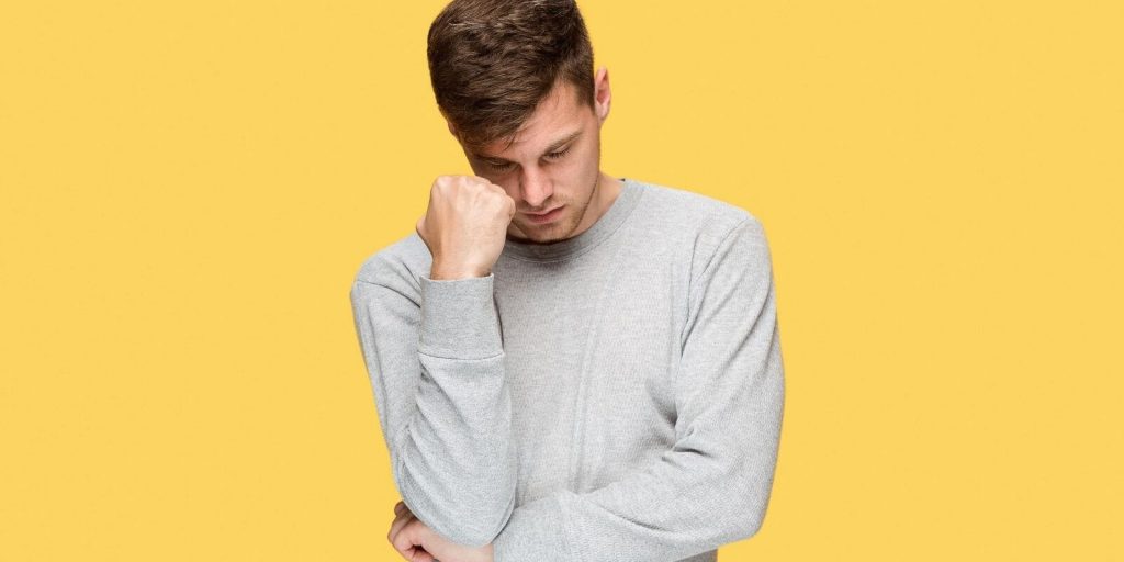 Image of a young man in stress standing across a yellow wall