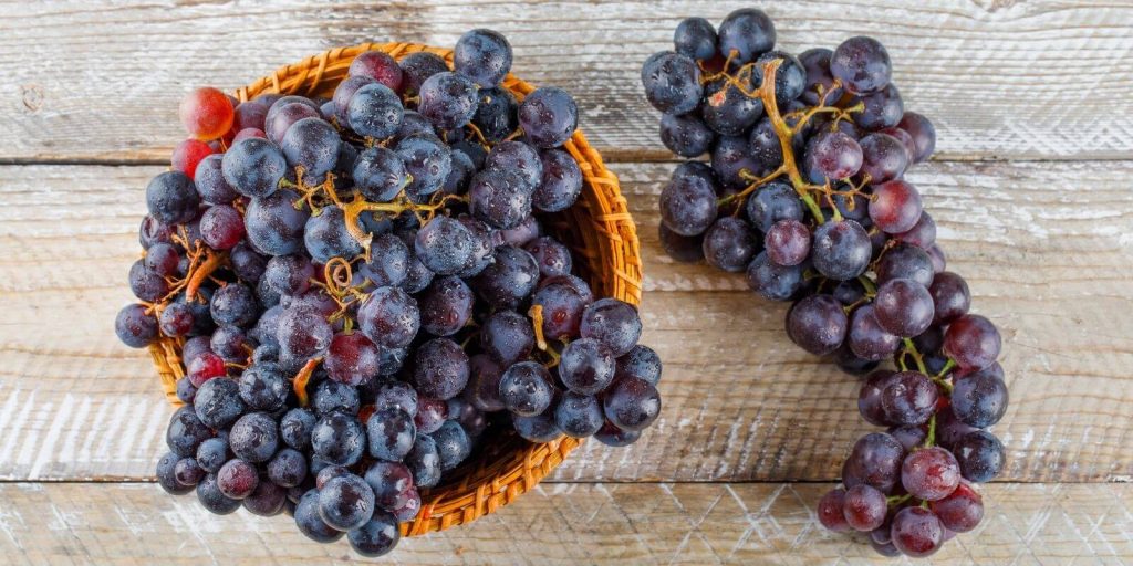 Purple grapes in basket on a wooden background