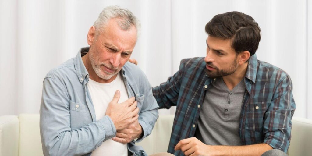 Old man experiencing chest pain and muscle tension sitting besides a young man