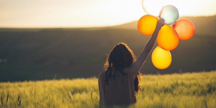 A happy person with baloons in the green valley