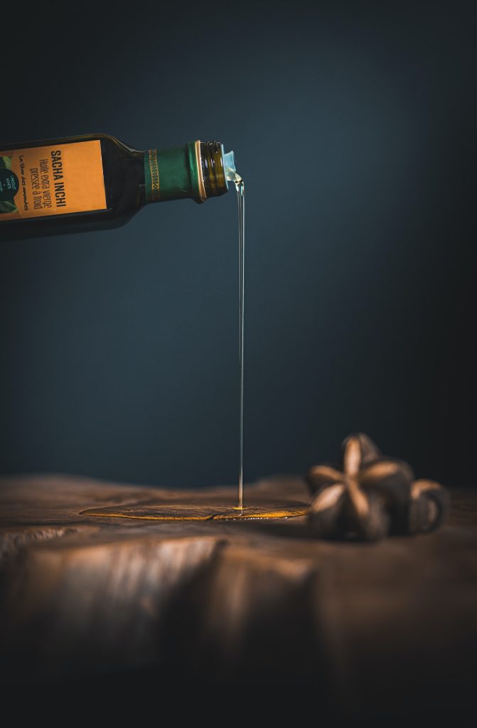 A bottle of olive oil being poured over a wooden pan