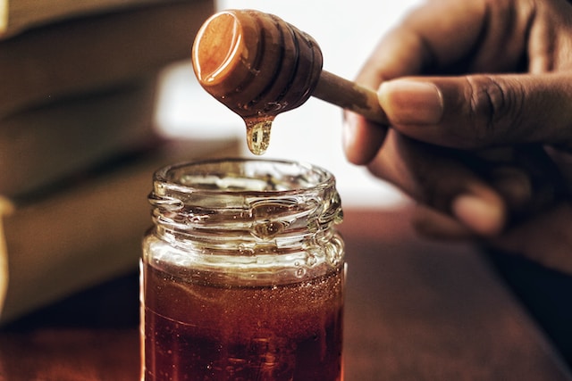 A person taking out honey from a honey jar with the help of honey dipper